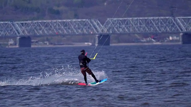 慢镜头:一只雄性风筝运动员在一条大河的水面上跳跃。水花溅向不同的方向。阳光明媚的春日。视频素材