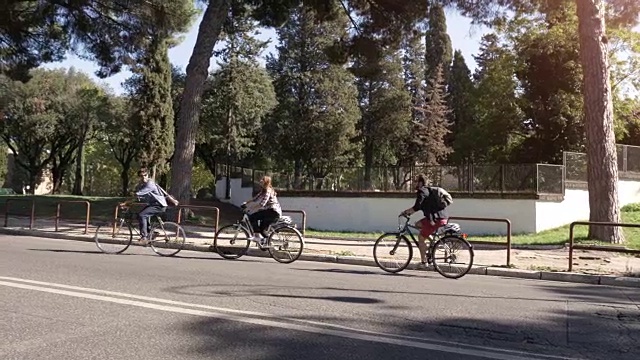 三个年轻的朋友游客在colle oppio公园骑自行车在罗马城市中心的树木在阳光明媚的日子慢镜头汽车稳定摄影机视频素材