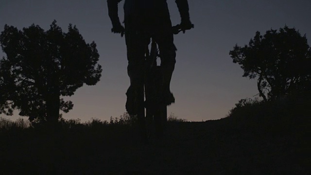 一个男人骑着山地车上山在沙漠剪影视频素材