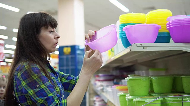 一位年轻的妇女在超市挑选并购买了一个塑料碗。视频素材