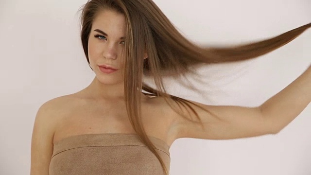 美丽的金发女孩裸露的肩膀玩头发对着白色的墙壁特写视频下载