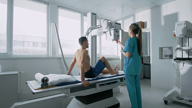 在医院里，男人坐在床上，女技术员调整x光机扫描他的腿受伤。扫描骨折，断肢，受伤，癌症或肿瘤。拥有先进医疗设备和专业技术的现代化医院视频下载