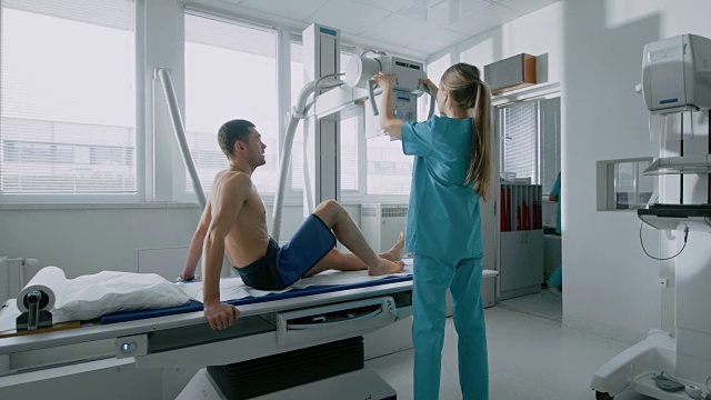 在医院里，男人坐在床上，女技术员调整x光机扫描他的腿受伤。扫描骨折，断肢，癌症或肿瘤。拥有先进的医疗设备和专业人才的现代化医院视频下载