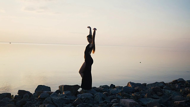 无忧无虑的女人穿着黑色长裙在日落时在海滩上跳舞视频下载