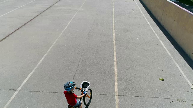 男孩在柏油路上戴着头盔骑着自行车，鸟瞰图视频下载
