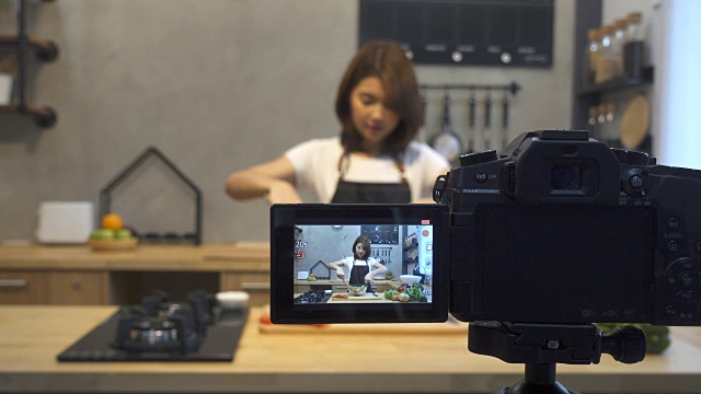年轻的亚洲女人在厨房里给摄像机录像。微笑的亚洲女人工作的食物博主概念与水果和蔬菜在厨房。视频下载