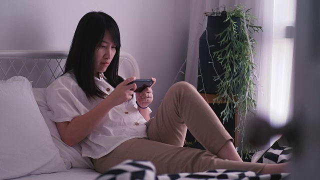 现代生活的泰国女人在她的卧室里玩智能手机游戏视频素材