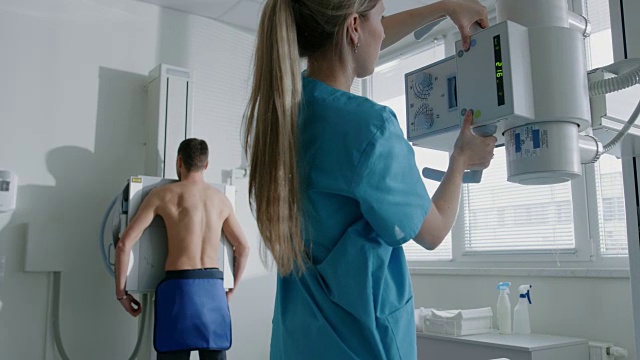 在医院里，当医务人员调整x光机进行扫描时，一个人脸靠墙站着。扫描骨折，断肢，胸部，癌症或肿瘤。拥有先进医疗设备的现代化医院。视频下载
