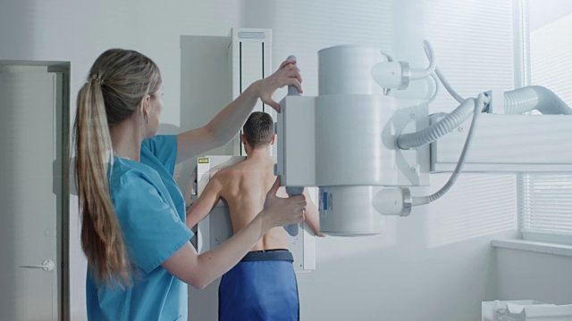 在医院里，当医务人员调整x光机进行扫描时，一个人脸靠墙站着。扫描骨折，断肢，胸部，癌症或肿瘤。拥有先进医疗设备的现代化医院。视频下载