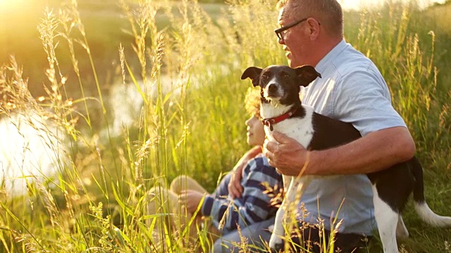 家庭，世代，沟通和人的概念-祖父和孙子与他的狗坐在河边的泊位上聊天。幸福的家庭度假视频下载