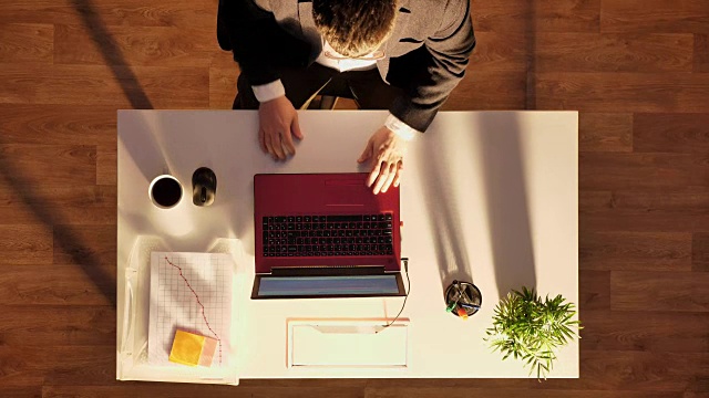 一个戴眼镜穿西装的年轻人坐在桌子后面拿着笔记本电脑和咖啡，准备离开，拍得好视频素材
