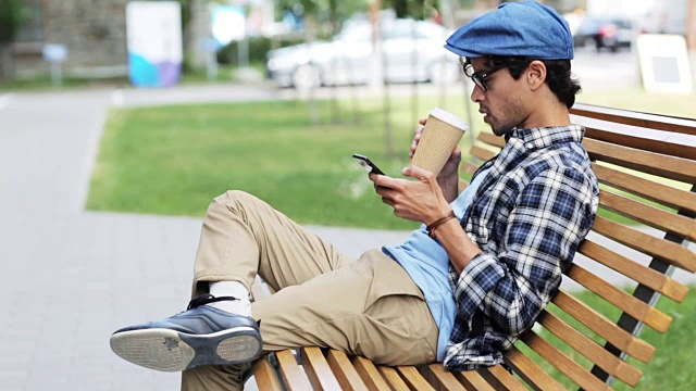一个拿着智能手机在城市街道上喝咖啡的男人视频素材