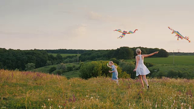 一个女人和她的女儿玩耍，她拿着一个空中风筝在兜圈子，女儿高兴地试图抓住他。快乐时刻的生活理念视频素材