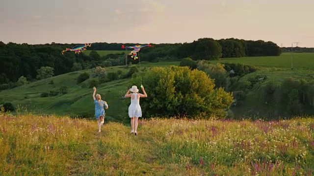 后视图:女人和一个拿着风筝跑的女孩。快乐的妈妈和女儿的概念视频素材