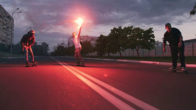 一群年轻人在清晨的马路上玩滑板，伴随着红色的信号弹，慢动作视频素材