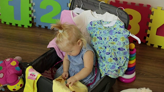 旅行和家庭度假。一个小孩正坐在装着衣服的手提箱里。视频下载