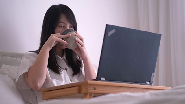 一名日本女记者正在喝热咖啡，同时在她的卧室里用电脑工作，在家里自由职业的工作过程视频下载