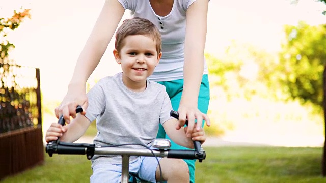 微笑的母亲教她的儿子在大自然骑自行车视频下载