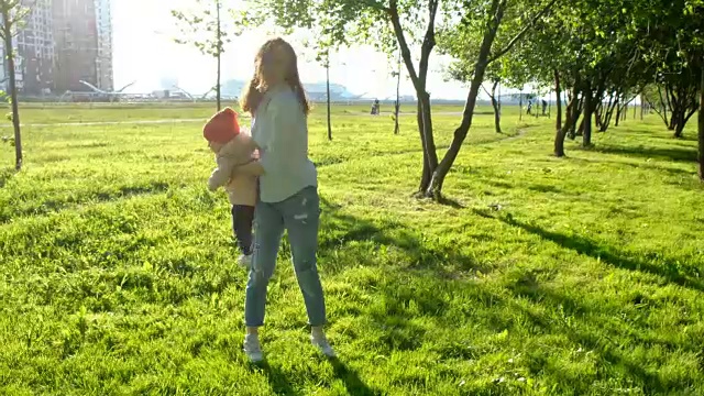 年轻的母亲和她的孩子在公园里转圈。快乐的家庭在夕阳下玩耍视频下载