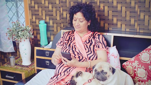 一个女人和她的宠物狗坐在床上玩智能手机。视频下载