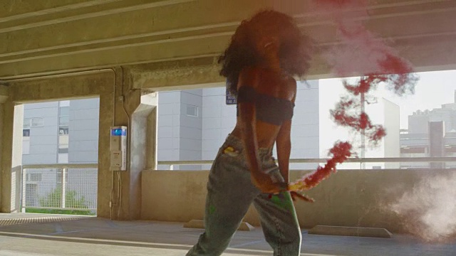 一名年轻女子的剪影与五颜六色的红色烟雾弹在停车场跳舞视频素材