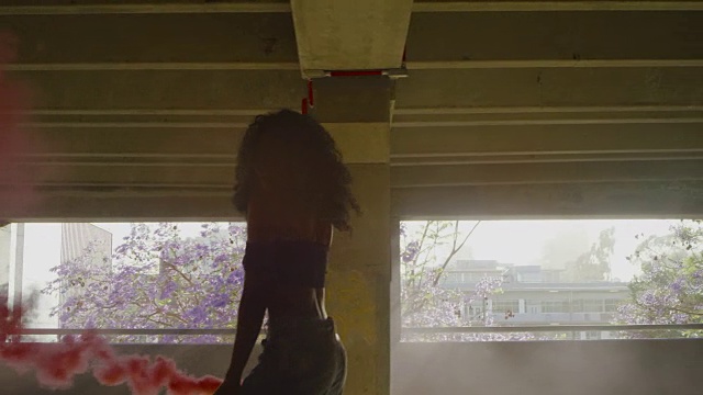 一名年轻女子的剪影与五颜六色的红色烟雾弹在停车场跳舞视频素材