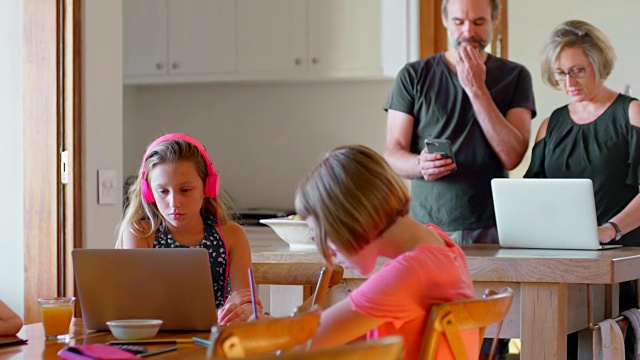 家长使用笔记本电脑和手机，而孩子在厨房学习4k视频素材