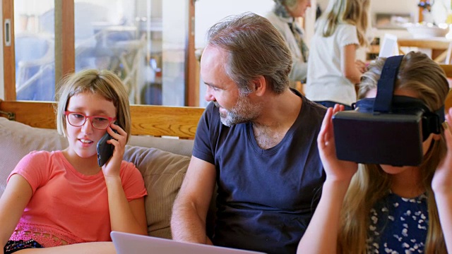 父亲用笔记本电脑，而女儿在客厅用手机讲4k视频素材