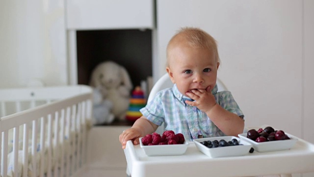 可爱的小男孩，在家吃新鲜水果，坐在儿童房的婴儿椅上。视频下载