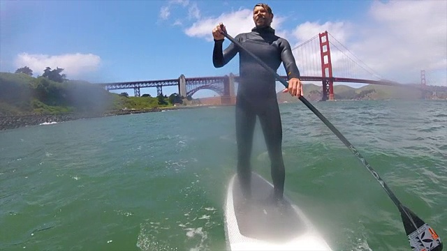 一个男人在金门大桥下直立划桨。——慢动作视频素材