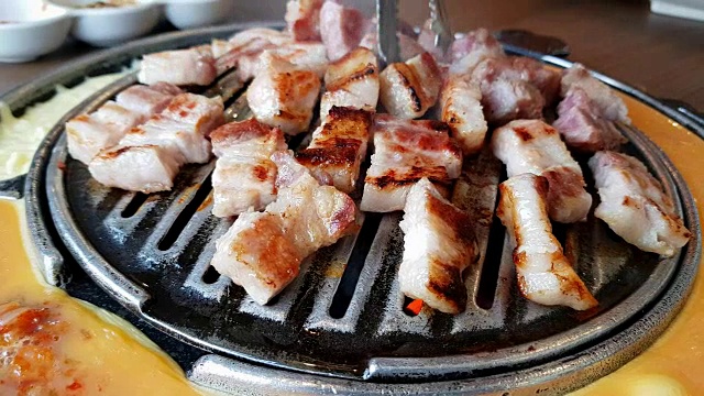 将猪肉切片放在平底锅和夹钳上烤和烧烤。平底锅的一边有煎蛋卷和奶酪。韩国烤肉(烧烤)视频购买