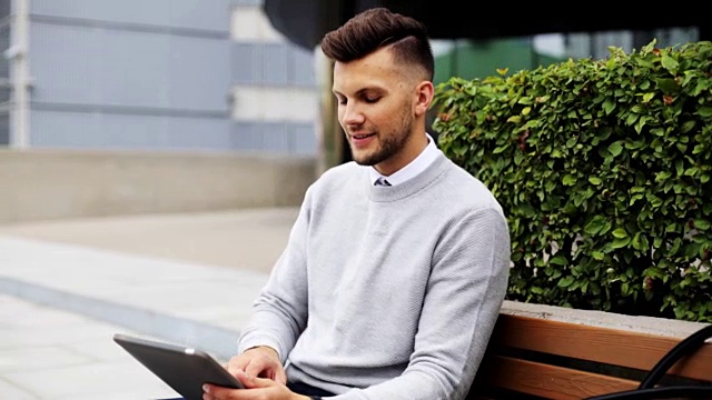 一个人拿着平板电脑坐在城市街道的长椅上视频素材
