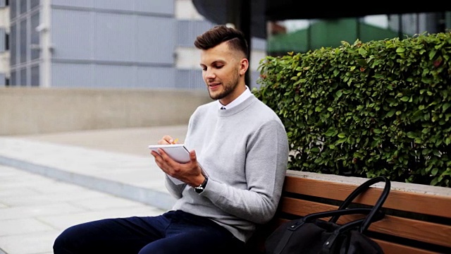 一个人拿着平板电脑坐在城市街道的长椅上视频素材