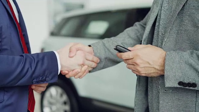 在成功地与销售经理握手后，男性手拿车钥匙的特写镜头。买卖汽车，商人握手的概念。视频下载