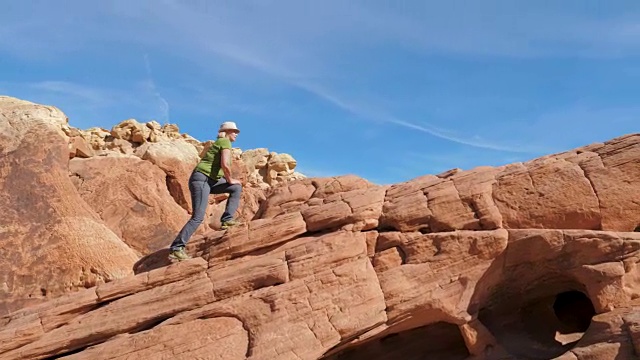 侧视图一个女人爬上红色的岩石背景天空视频下载