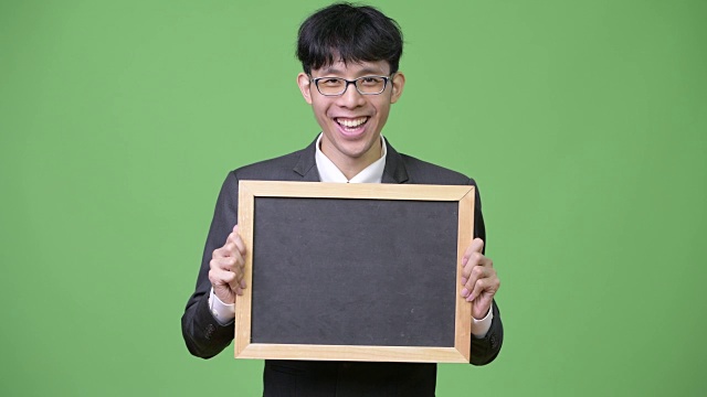年轻快乐的亚洲商人微笑着向镜头展示黑板视频下载