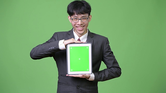 年轻快乐的亚洲商人向相机展示数码平板电脑视频下载