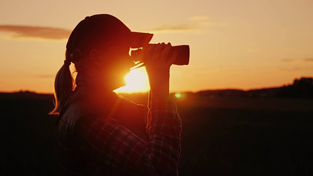 一个用双筒望远镜看日落的女人。旅行和狩猎概念视频下载