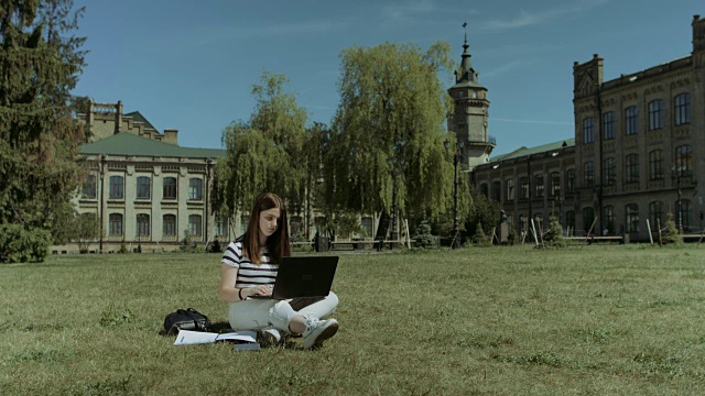 漂亮的女学生在草坪上用笔记本电脑工作视频素材
