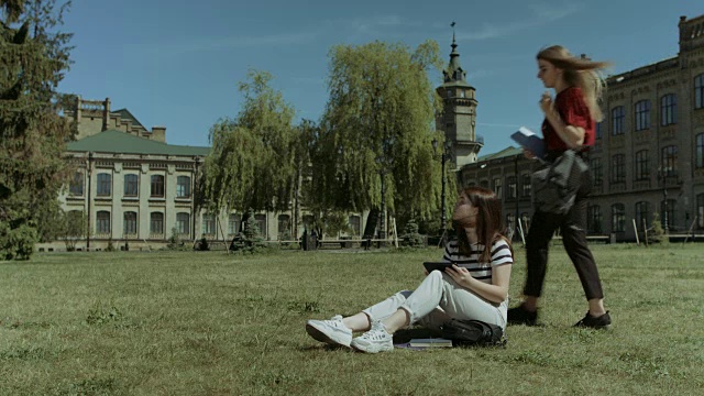 两个女大学朋友在校园草坪上见面视频素材