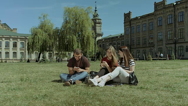 带着微笑的学生们在草坪上用智能手机交流视频素材
