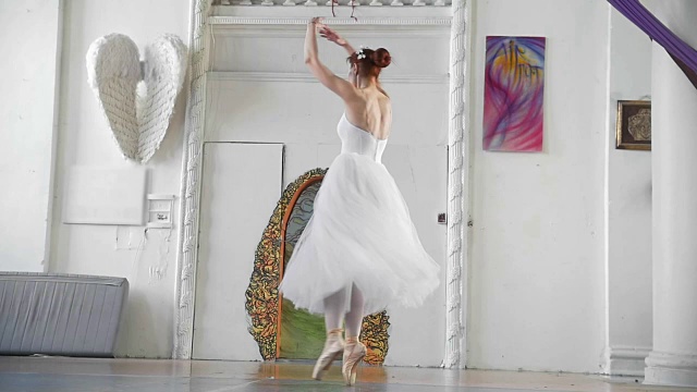 年轻迷人的芭蕾舞女演员穿着白色芭蕾舞裙在宽敞的工作室里跳脚尖旋转视频素材