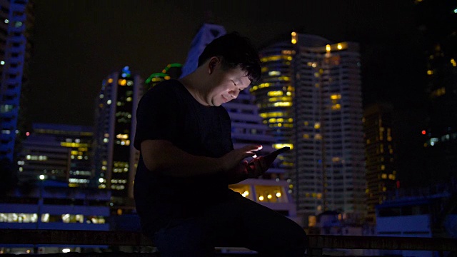 年轻人晚上在城市里低头看智能手机视频素材