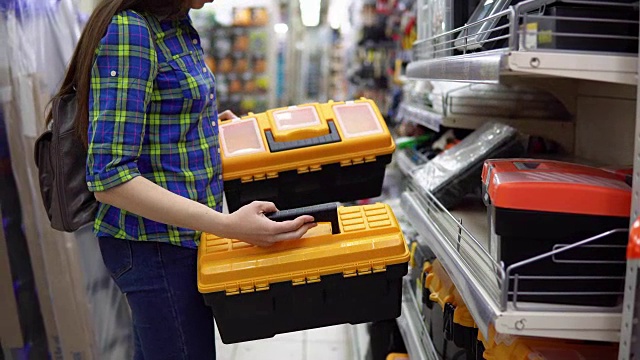 一个年轻的女人在商店里选择了一个塑料工具箱。视频素材