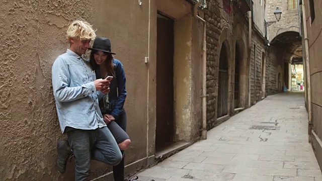 在城市狭窄的街道上，一对年轻夫妇正用手机看社交媒体视频素材