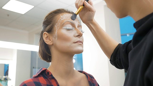 一位专业的化妆师在模特的脸上画身体艺术。准备参加选美比赛。视频下载