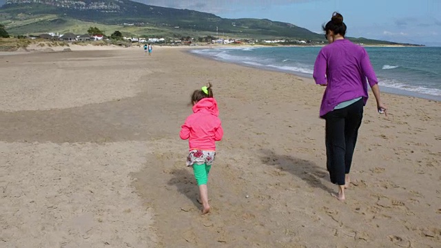 女孩和妈妈在海滩上寻找贝壳视频素材
