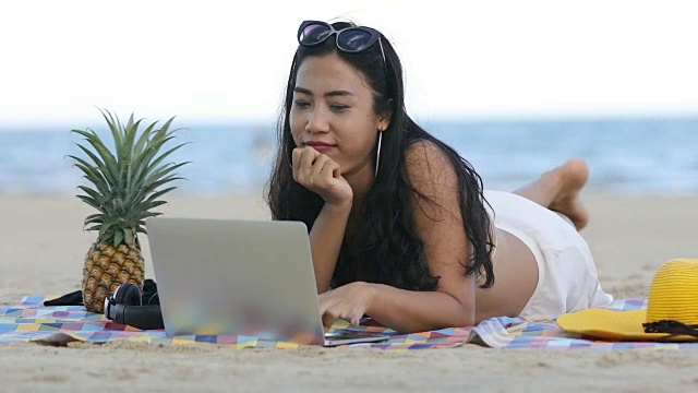 穿着比基尼的女性在夏天用笔记本电脑工作，在海滩上听音乐。视频下载