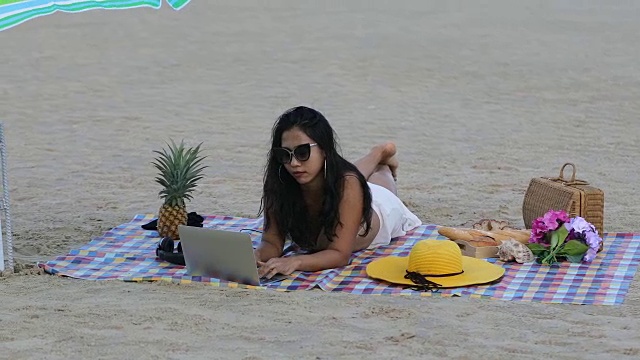 穿着比基尼的女性在夏天用笔记本电脑工作，在海滩上听音乐。视频下载