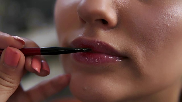 一个女人的嘴唇用唇彩的特写镜头。化妆师用薄薄的专业刷子涂抹唇彩。构成概念视频素材